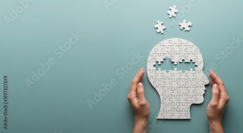 Hands holding a human head shape made of puzzle pieces with some pieces missing against a blue background