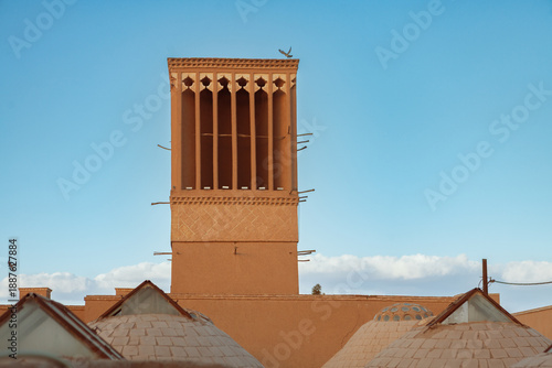 Картината върху платно A wind catcher (badgir) rises above traditional domed rooftops, set against a bright blue sky