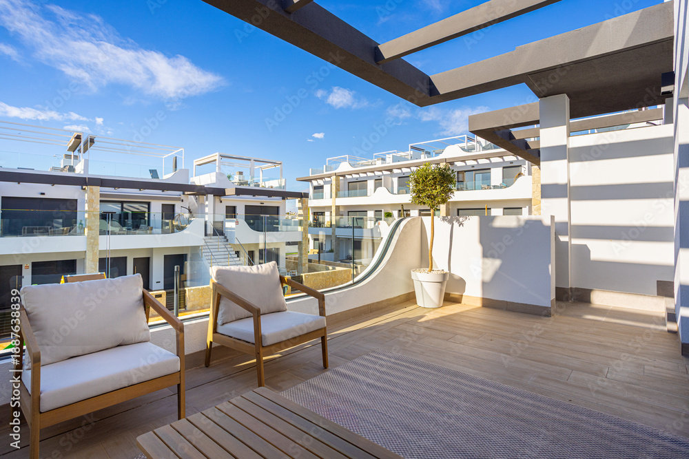 Naklejka premium Modern apartment terrace with outdoor lounge seating and sunny view of residential complex