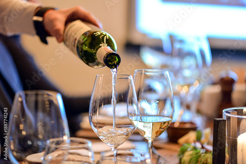 The waiter pours white wine into a glass