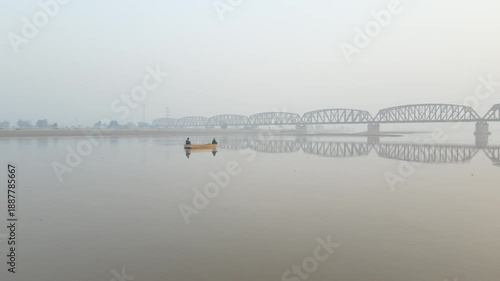 Fishermen in a boat, sailing on the water of a river, with a huge bridge in the background. Drone Video, 4K, Aerial Panning Shot.