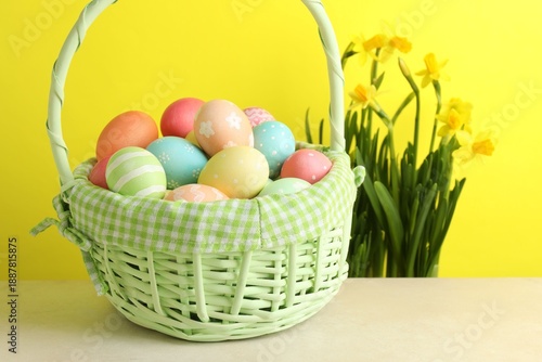 Wallpaper Mural Painted Easter eggs in wicker basket on beige table and daffodils against yellow background, closeup Torontodigital.ca