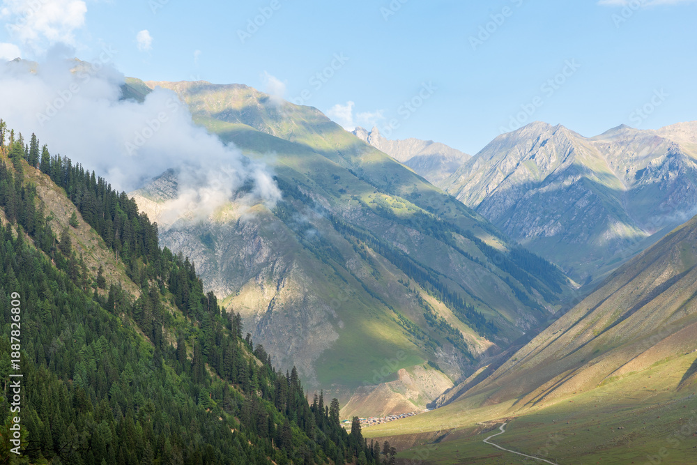 Fototapeta premium Untouched valley in northern areas of Pakistan surrounded by mountains with low hanging clouds and lush green views