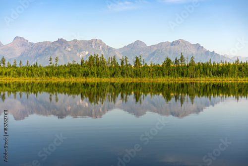 Φωτογραφία Serene mountain lake Tayozhnoye near Chara sands with clear reflection of Kodar mountain range and forest on water surface