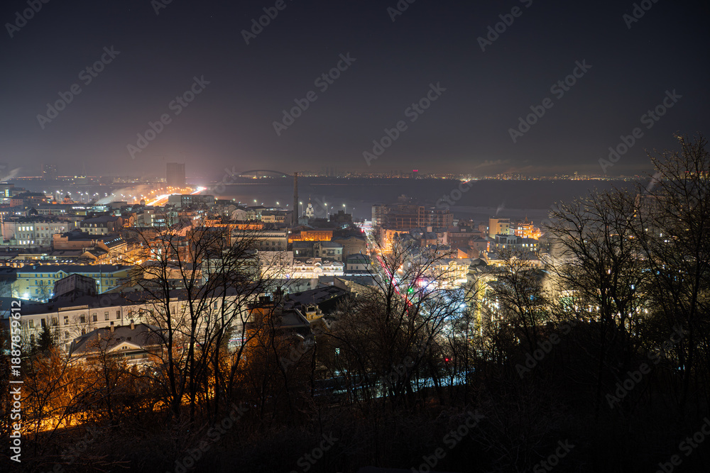 Naklejka premium Nighttime cityscape of Kiev, Ukraines Podil district Layered buildings with contrasting white and yellow lights, viewed from an elevated position The composition emphasizes depth and light contras
