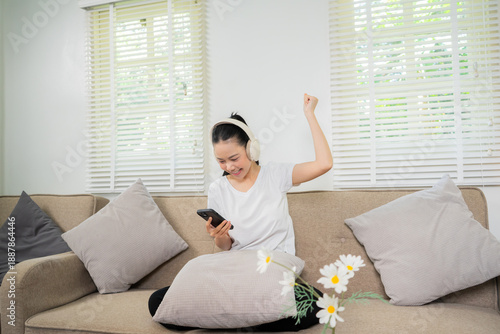 A young woman is relaxing on the sofa at home, smiling, holding a cup of tea, enjoying a peaceful weekend. The warm and cozy atmosphere of the living room, a relaxed lifestyle, and a blissful daydream