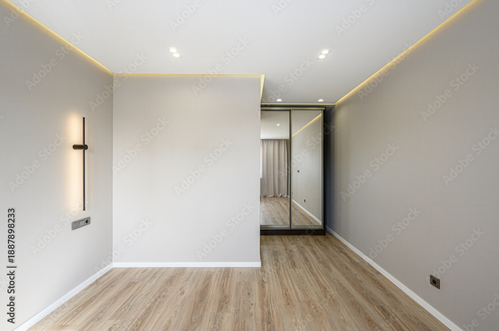 Obraz premium Modern minimalist room with light wooden flooring, neutral walls, recessed ceiling lights, LED strip, sleek wall lamp, mirrored wardrobe, clean lines, spacious layout.