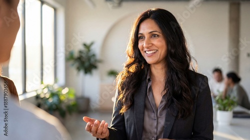 Smiling businesswoman speaking in modern office with natural light and plants, confident conversation conveying warmth and professionalism