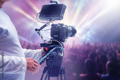Video production operator films a live concert with a professional camera on tripod. Event recording and media coverage by a videographer. Entertainment and broadcast services.