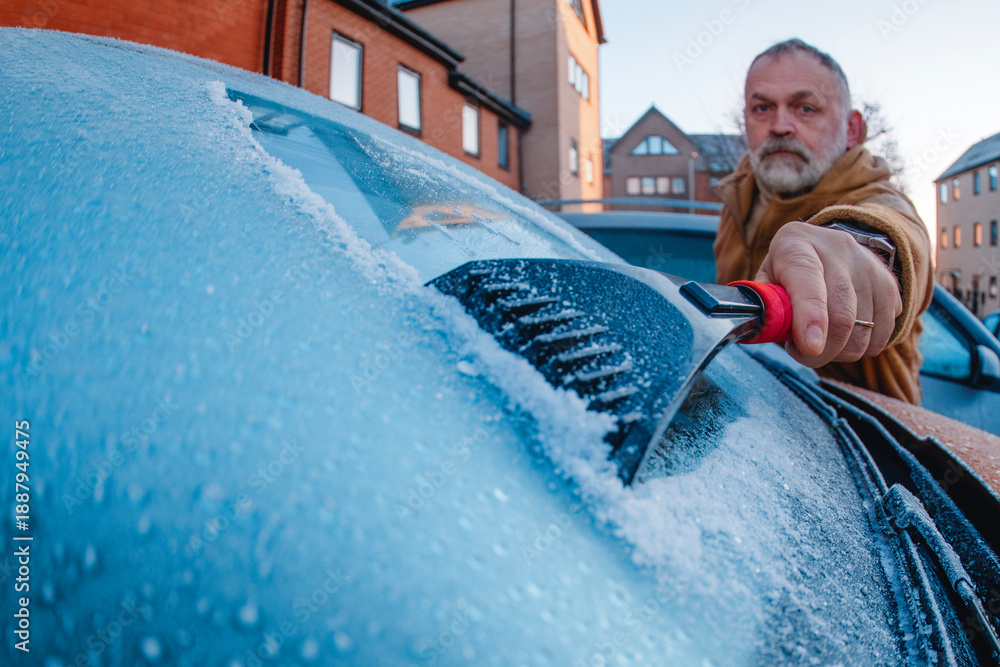 Ταπετσαρία Man scrapes ice off car windshield in urban area during early morning frost