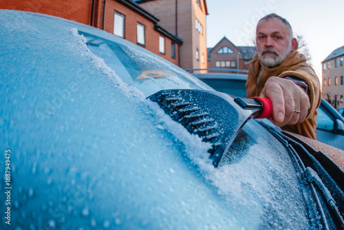 Billede på lærred Man scrapes ice off car windshield in urban area during early morning frost