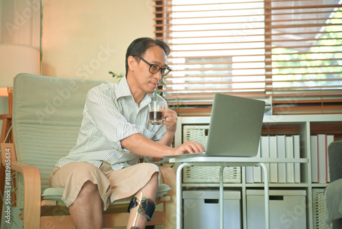 Middle-aged man working on a laptop at home while wearing a prosthetic leg, focused remote work