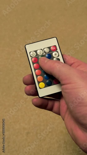 Hand holding a remote control with color selection buttons and on/off switch