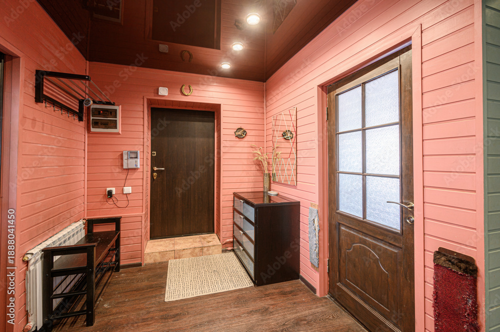 Fototapeta premium Cozy hallway with pink wooden paneling, dark wood doors, built-in storage unit, radiator, shoe rack, frosted glass door, decorative wall elements, woven rug.