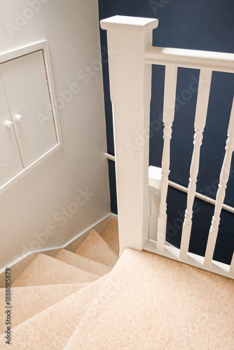 Looking down a contemporary stairwell featuring cream carpet, white painted woodworking, and a dark blue accent wall