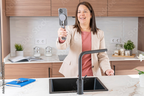 Female realtor filming a home tour video with a mobile phone in a stylish kitchen