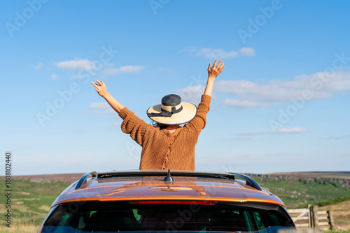 Fotografie Enjoying freedom on a sunny day with a hat while sitting on a car roof