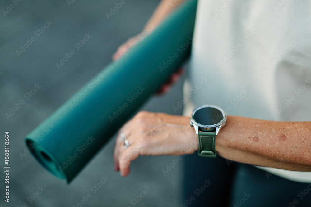 Fototapeta premium Portrait of a mid age mature sport woman smiling happy and confident, prepering for jogging and run looking at her watch and performance. Running in city park outdoors