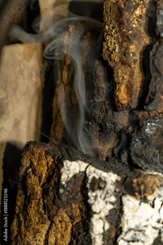 Burning firewood logs with smoke rising between charred wooden pieces. Close-up outdoor fire texture photography. Wood combustion and heat source concept for design for poster, banner, wallpaper