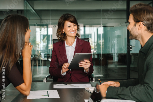 Photos Smiling gesturing female corporate boss manager holding tablet, presents project to collaborative colleagues or client