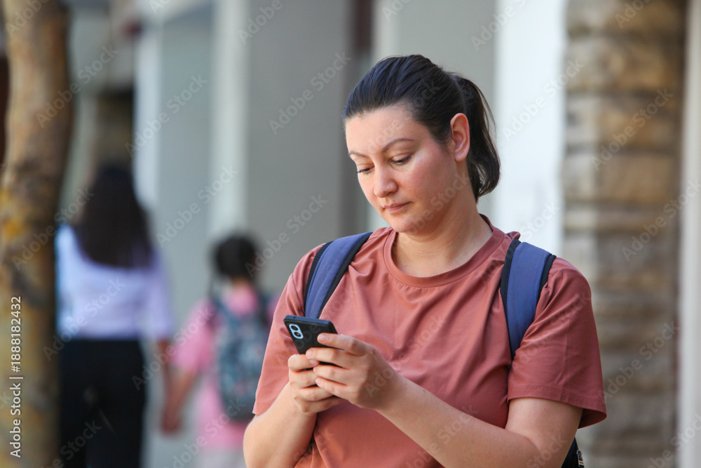 Φωτογραφία Close-up urban lifestyle portrait of an adult woman with backpack  using a smartphone on a city street