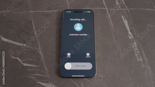 A smartphone sits on a table showing an incoming call. The caller's identity is unknown. The phone displays options to answer or decline the call.