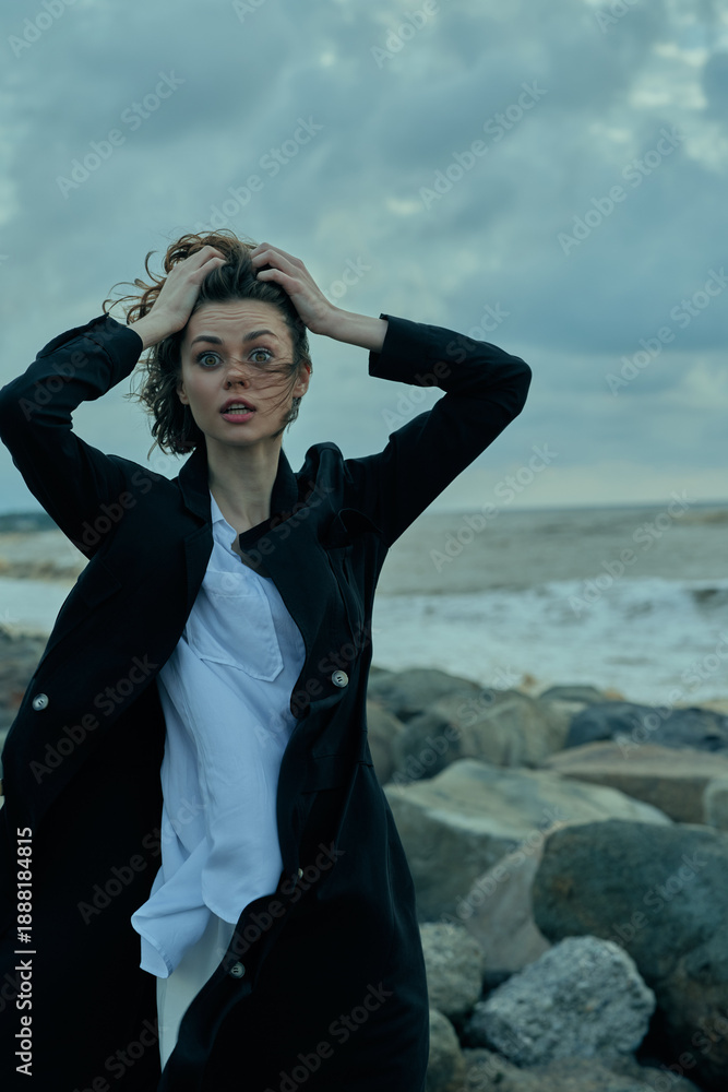 Φωτογραφία Windy beach scene with windblown hair, stormy sky, and a woman in a black coat a