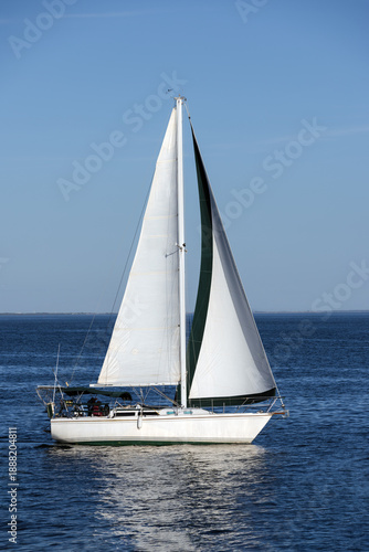Sailboat with white sails on calm blue sea under clear sky