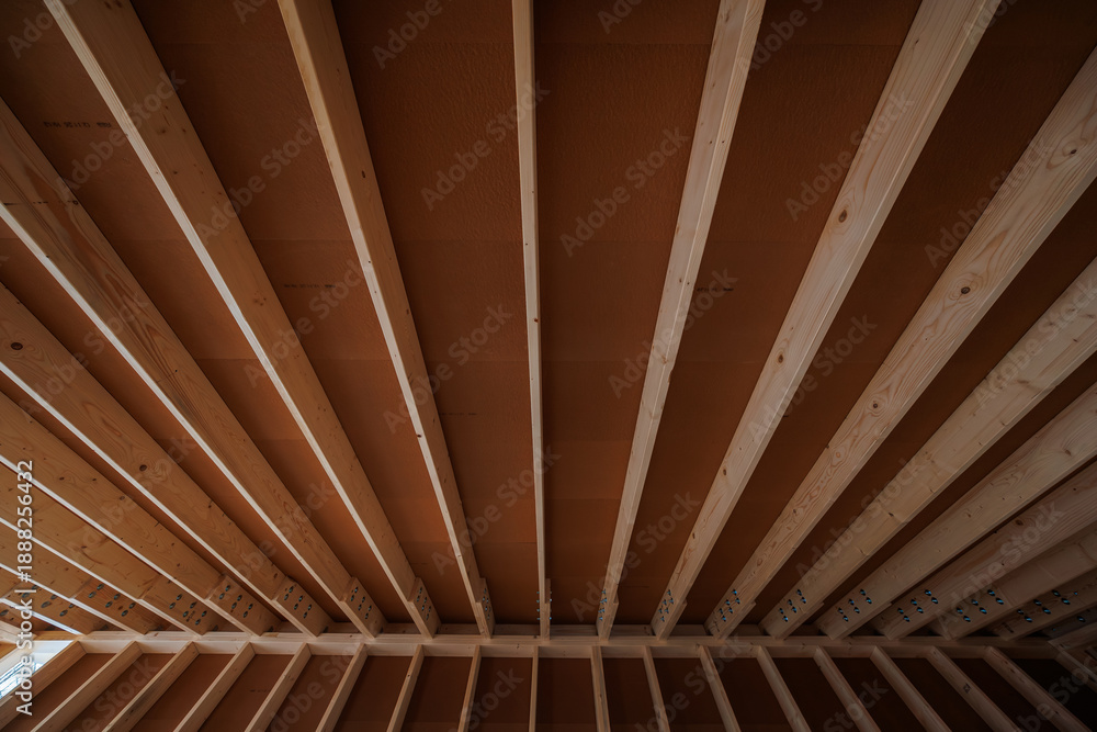 Obraz premium Close up view of unfinished timber framing with evenly spaced roof joists and sheathing panels, rows of metal nails and brackets, daytime, warm wood tones, wide angle.