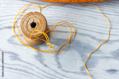 Slika na platnu Top view of a yellow thread spool with loose thread on a light wooden tabletop w