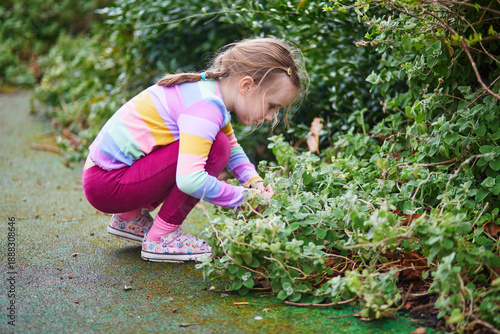 Bilde på lerret Curious young girl in a colorful striped sweater squatting down and examining gr