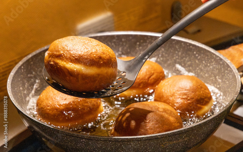 Taking out fresh golden doughnut from hot frying oil with skimmer spoon for traditional Fat Thursday dessert preparation and delicious homemade sweet pastry cooking.