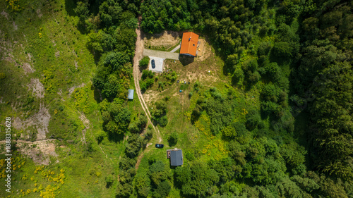 Aerial rural homestead with red orange roof amid forest and meadow