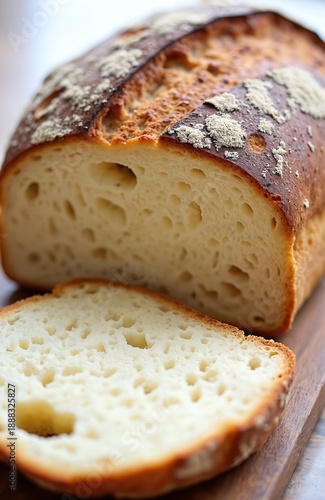 Freshly baked artisan bread on wooden board. Crusty loaf sliced revealing soft white crumb. Delicious homemade bakery food, perfect for breakfast or any meal.