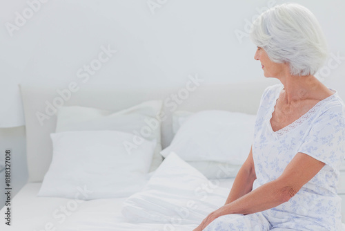 Upholstered bed with layered white pillows and folded duvet is sitting in bright bedroom near lamp