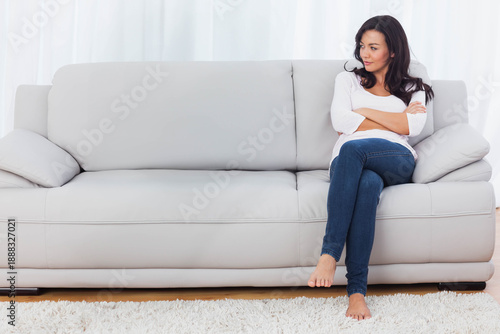 Foto Woman in 20s sitting on right of light-gray sofa, wearing white top, jeans, bare