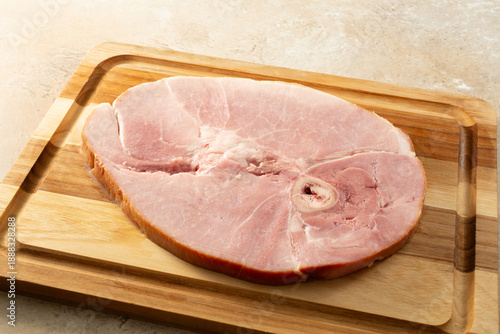 A view of a cooked bone in ham steak, on a wood board.