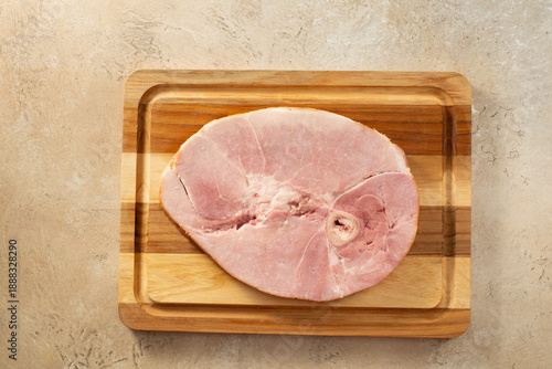 A top down view of a cooked bone in ham steak, on a wood board.