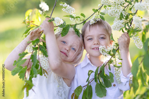 A little girl and a boy are smiling at the camera from among the branches of a flowering tree