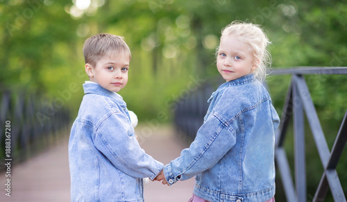 A little boy and a little girl are walking hand in hand across a bridge and look back at the camera