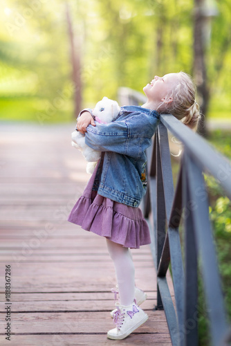 a little girl is laughing  standing on the bridge, hugging a toy