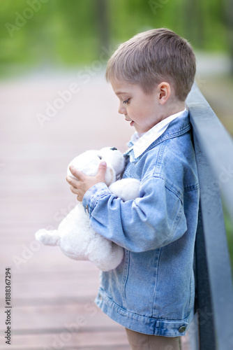 a lonely little boy is standing on a bridge and hugging a toy puppy