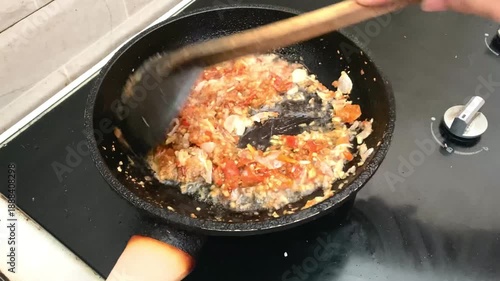 stir frying spicy chili and onion paste in a black frying pan on a modern electric stove