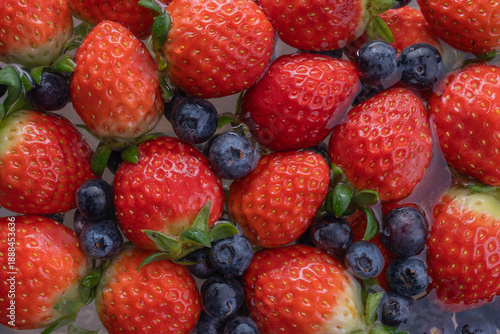 Fresh strawberries and blueberries soaking in water, vibrant red and deep blue colors, juicy texture, healthy summer fruit background.