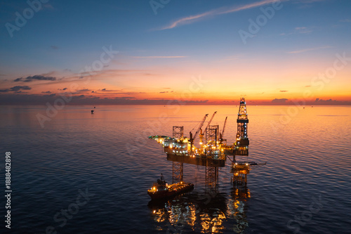 Aerial view from a drone of big jack up offshore drilling oil rig, production platform and supply vessel In the ocean during sunset - Oil and Gas Industry
