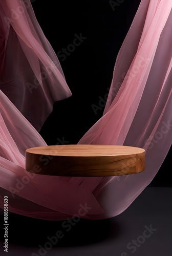 Elegant wooden podium showcasing a refined aesthetic, gracefully framed by a flowing sheer pink fabric on a deep dark background, perfect for stylish product display and luxurious presentation