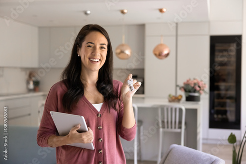 Portrait of smiling real estate agent, professional female realtor holds house keys and digital tablet, standing in modern kitchen. Successful property deal, housing market, investment, home ownership