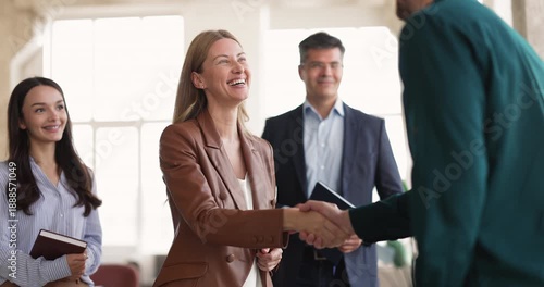 Happy businesswoman greeting male client during group meeting in office, handshaking, closing successful deal, approving partnership. Business relationship building, consulting services, agreement