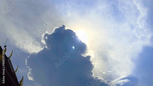 The Sun's Shining Behind Big Cloud and Bird on Part of Roof of Temple on Blue Sky Background with Bird Flying Compound of a Monastery at Bangkok, Thailand. 19 MAY 2025, A.M./ Real Time Video
