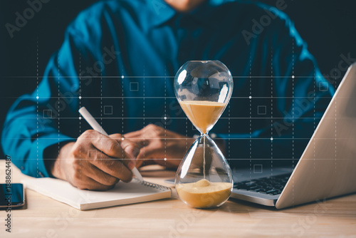 Canvas Print Man writing ideas in book, watching hourglass time for business work, sandglass